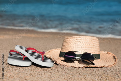 Striped flip flops, straw hat and sunglasses on sandy beach near sea