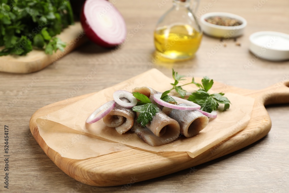 Board with delicious salted herring fillets, onion rings and parsley on wooden table Board with delicious salted herring fillets, onion rings and parsley on wooden table