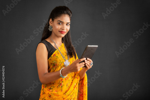 Young beautiful girl or woman holding and using smartphone or mobile or tablet phone on a grey background