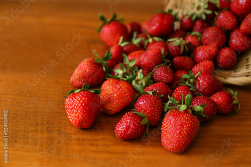 Basket with scattered ripe strawberries on wooden table, closeup