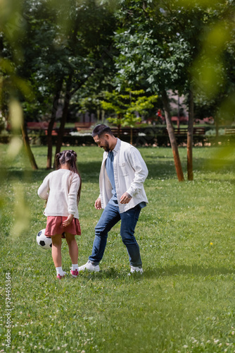 Cheerful asian man playing football with preteen daughter in park.