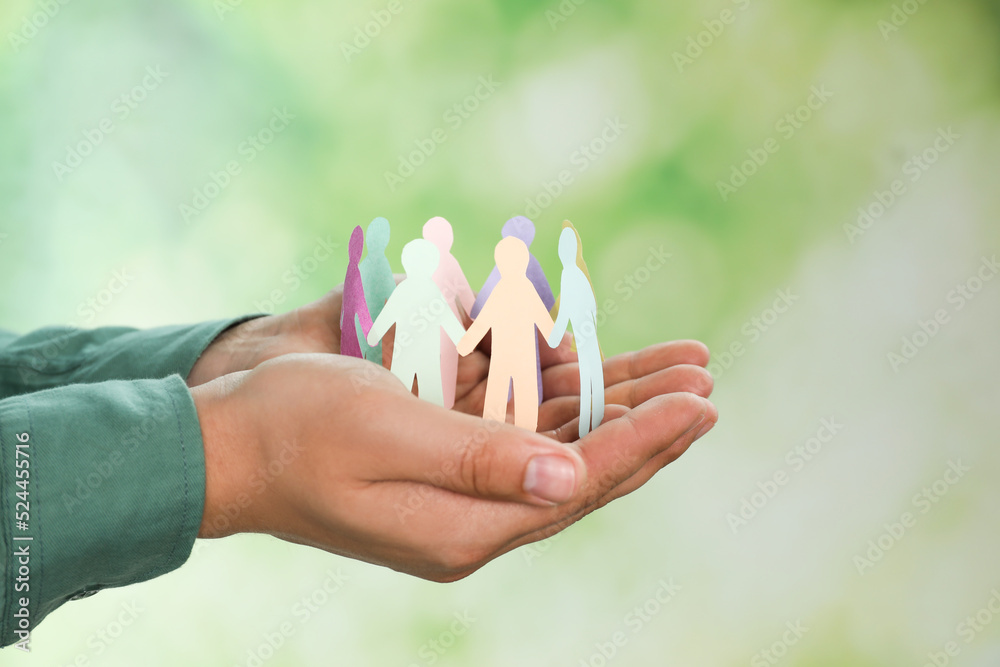 Man holding paper human figures on blurred background, closeup. Diversity and Inclusion concept - obrazy, fototapety, plakaty 