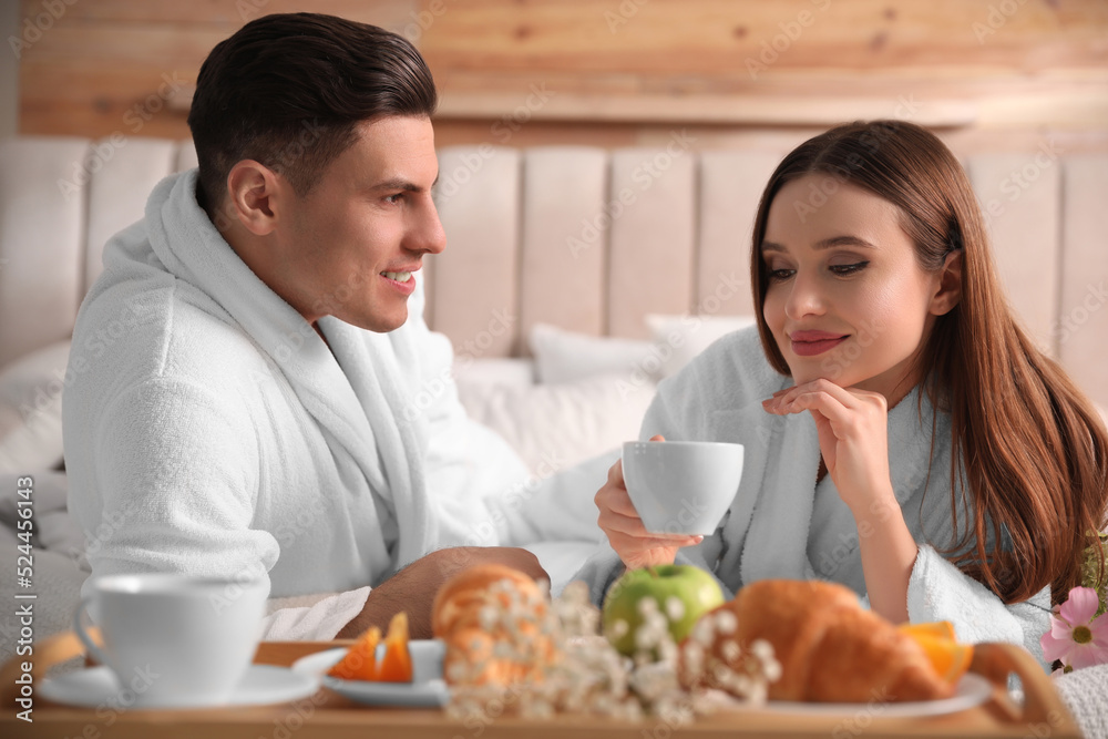 Happy couple in bathrobes having breakfast on bed at home