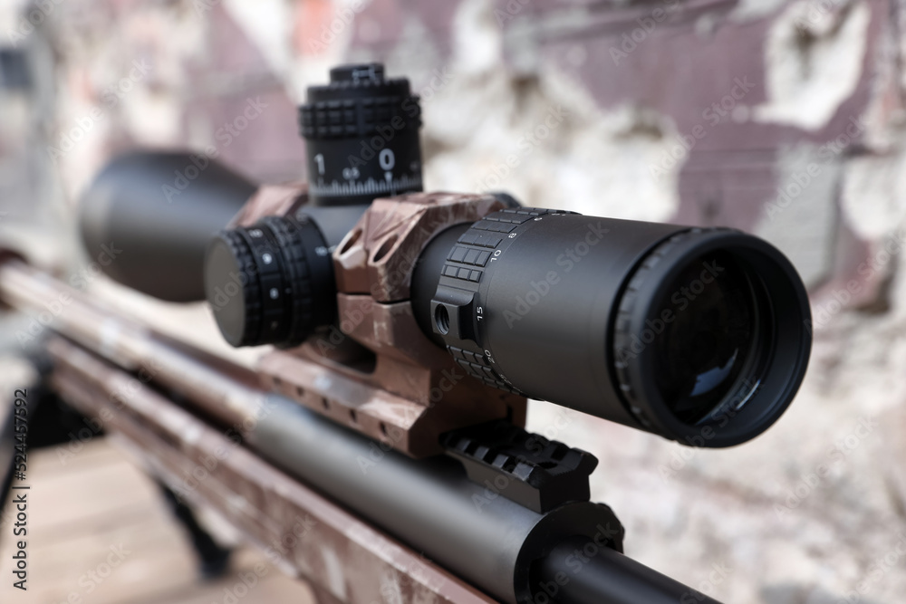 Closeup view of modern powerful sniper rifle with telescopic sight on blurred background