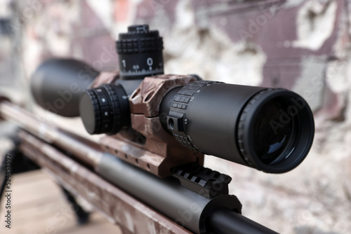 Closeup view of modern powerful sniper rifle with telescopic sight on blurred background