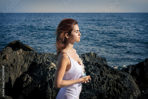 Peaceful lady with ship miniature in hands standing on rocky seashore