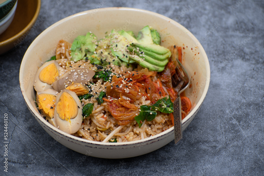 Korean brown rice, kimchi, stir fried vegetables and pickled egg, avocado in a bowl, copy space