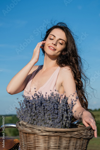 pretty brunette woman with long hair smiling near blurred lavender flowers.