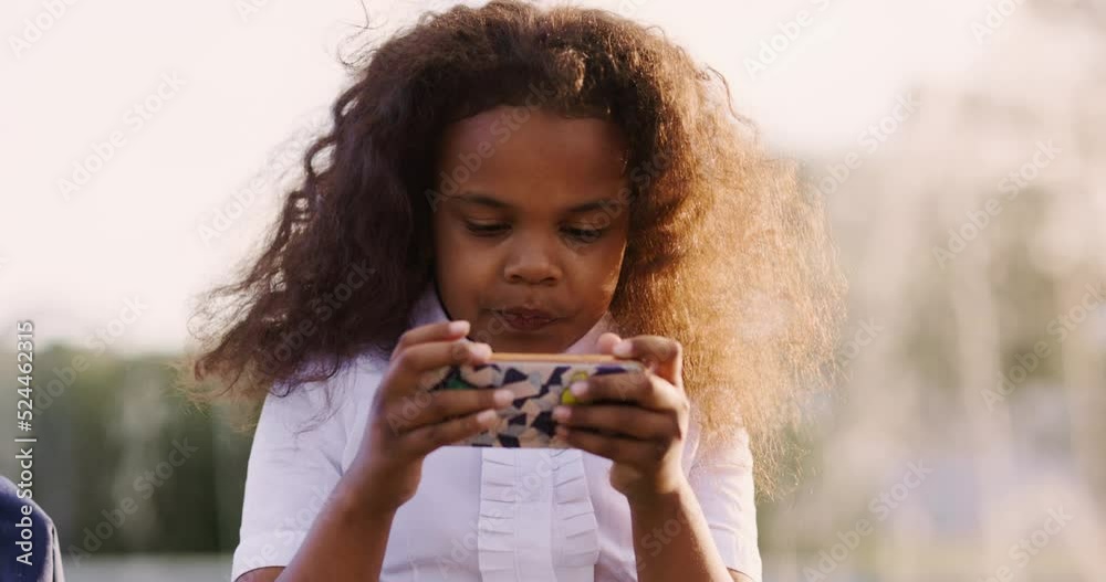 Teenage african american girl in school clothes with a smartphone plays a game application after studying at school Teenage african american girl in school clothes with a smartphone plays a game application after studying at school
