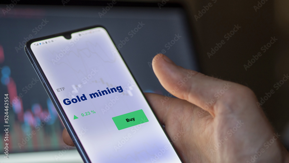 An investor's analyzing the gold mining etf fund on a screen. A phone shows the prices of gold mining An investor's analyzing the gold mining etf fund on a screen. A phone shows the prices of gold mining