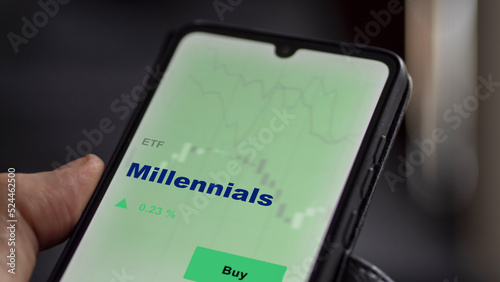 An investor's analyzing the millennials etf fund on screen. A phone shows the ETF's to invest
