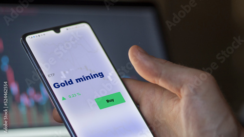 An investor's analyzing the gold mining etf fund on a screen. A phone shows the prices of gold mining