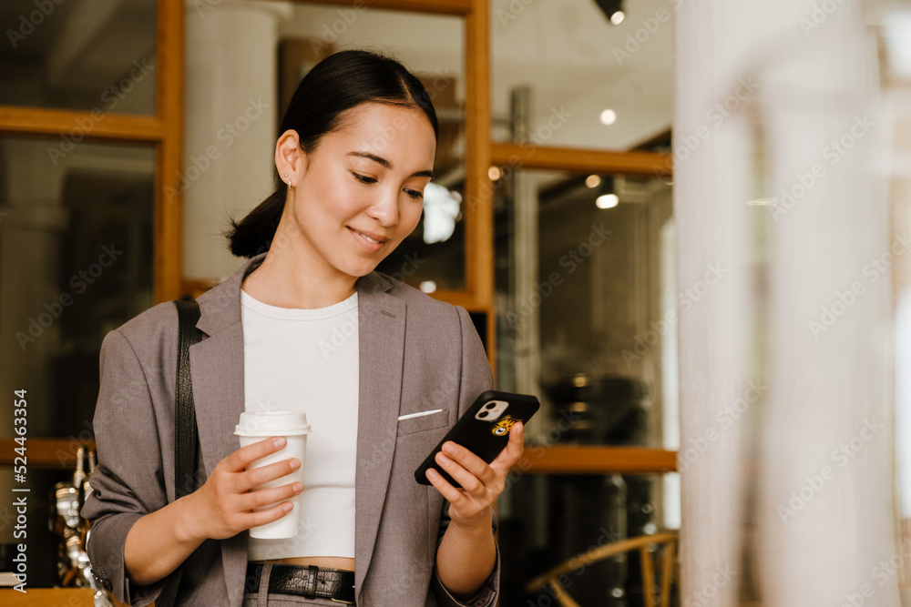 Asian businesswoman drinking coffee and using cellphone in cafe