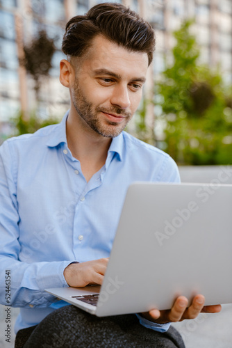 Bristle man working with laptop while sitting on stone bench