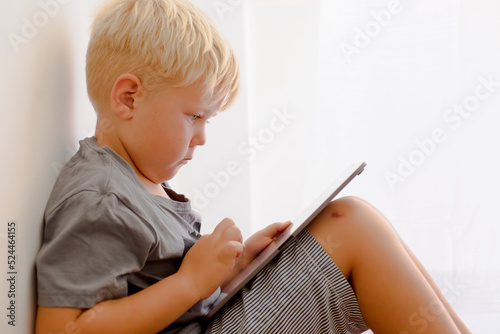 Fototapeta Blondy boy spend his leasure time in tablet