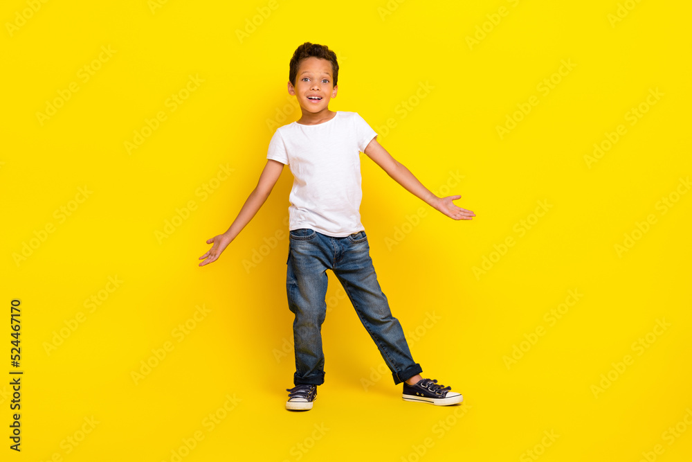 Full size photo of little boy stand wear t-shirt jeans shoes isolated on yellow color background Full size photo of little boy stand wear t-shirt jeans shoes isolated on yellow color background