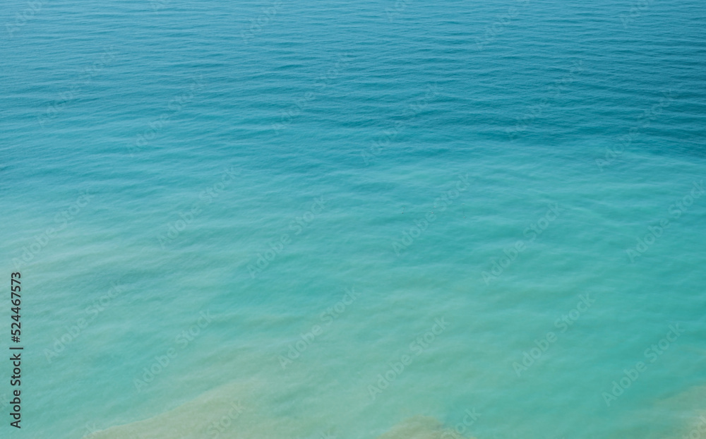 Obraz premium Blurred background of the sea in the midday heat from a bird's eye view. Hot summer vacation, pastel colors and reflections on the water. Abstract blur poster or advertising banner