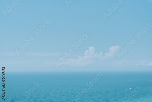 Sunny sky with clouds and a calm sea on a midday background. Soft blurry focus. Hot summer vacation, pastel colors and sun glare. Abstract blur poster or advertising banner