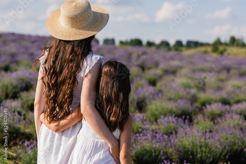 back view of woman and girl with long hair embracing in field.