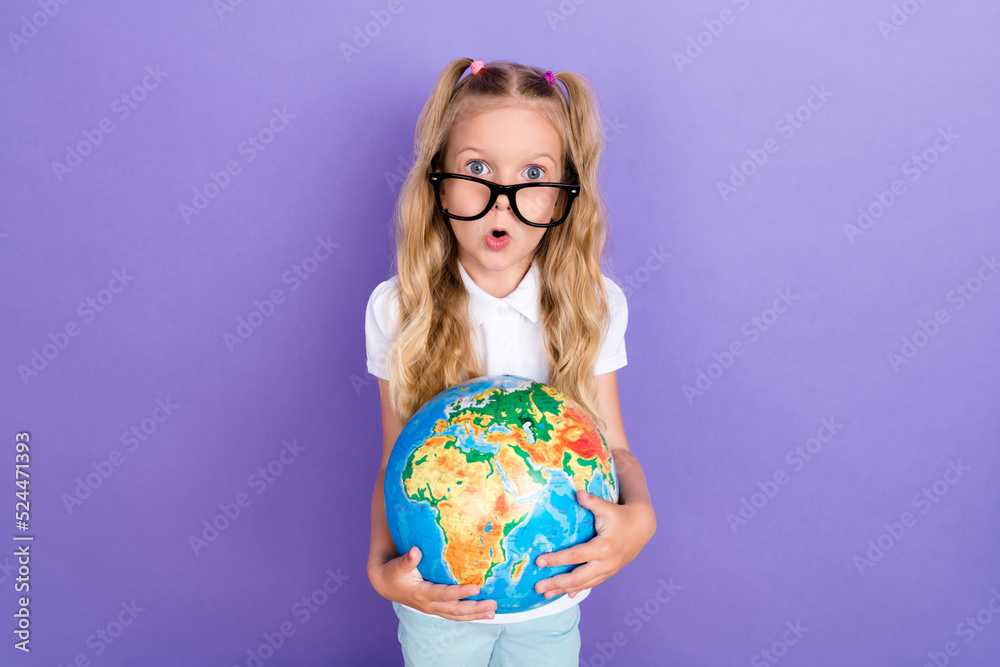 Photo of cute smart girl ponytails specs arms hold globe impressed new lesson wear trendy white blouse isolated on purple color background Photo of cute smart girl ponytails specs arms hold globe impressed new lesson wear trendy white blouse isolated on purple color background