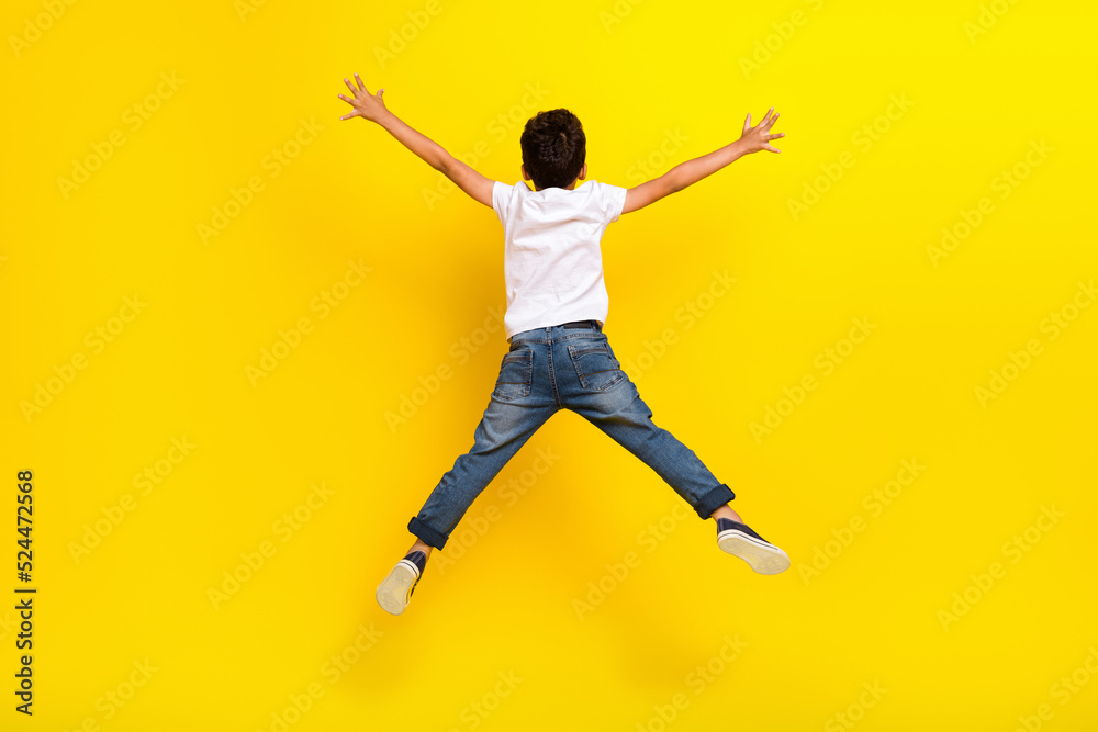 Full size back photo of little boy jump wear t-shirt jeans sneakers isolated on yellow color background