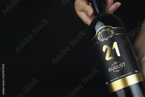 August 21st . Day 21 of month, Calendar date. Hands hold bottle of red wine with a calendar date on label. Summer month, day of the year concept.