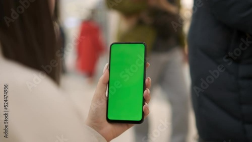 View of a woman on the phone with a green screen for copy space. Chromakey mockup without tracking markers. Close up.Young woman standing in a shopping mall with a smartphone. Busy shopping center photo