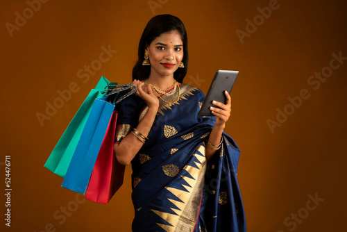 Portrait of a young woman with a mobile phone or tablet smartphone and shopping bags in her hands.