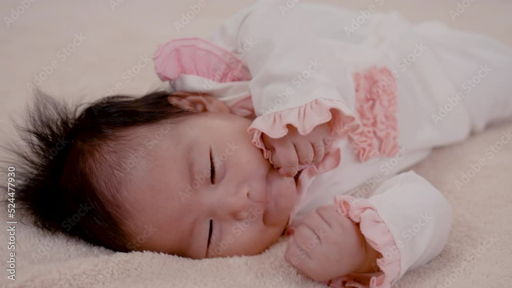 4K, Asian newborn baby girl 3 months old is lying on the bed with her hands clasped and releasing and covering her face happily while waiting for her mother to take care of her. 4K, Asian newborn baby girl 3 months old is lying on the bed with her hands clasped and releasing and covering her face happily while waiting for her mother to take care of her.