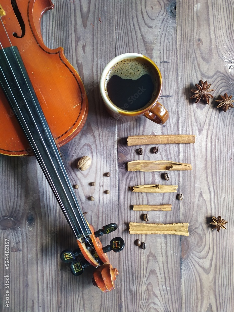 Naklejka premium Musical note chord of cinnamon, coffee beans, star anise, with cup of coffe and violin on brown wooden background, top view