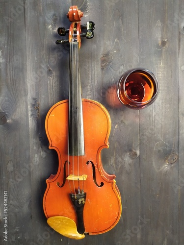 still life of violin and brandy or cognac glass, green plant on black wooden background