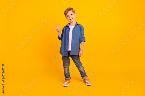 Full body photo of cheerful boy hand fingers demonstrate v-sign isolated on yellow color background © deagreez