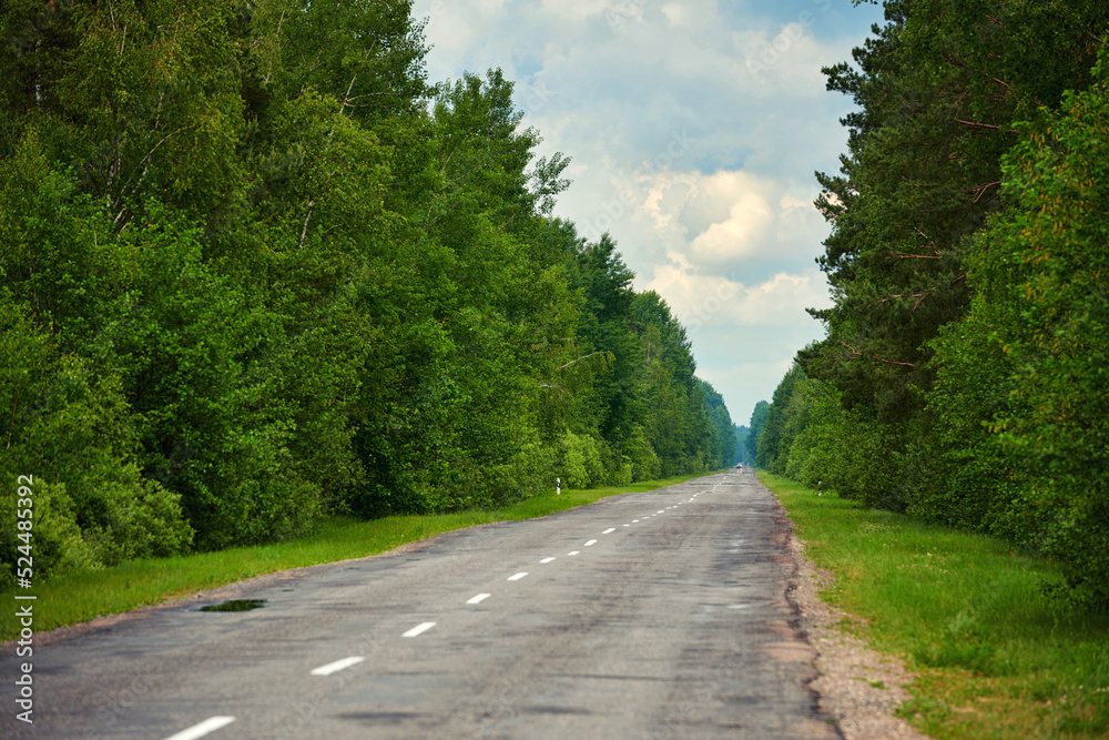 Road through the forest. Country road, path way through green summer forest. Driving car on asphalt forest road with one car on the horizon moving towards Road through the forest. Country road, path way through green summer forest. Driving car on asphalt forest road with one car on the horizon moving towards