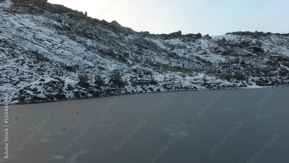 aerial dorne shots of a lagoon in an inactive volcano, frozen and with snow on the stones on the shores. aerial dorne shots of a lagoon in an inactive volcano, frozen and with snow on the stones on the shores.