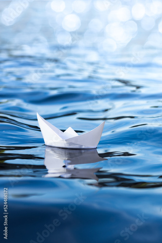 white paper ship on blue water, vertical frame, origami boat floats on the waves, concept of travel, holidays, symbol of freedom and dreams