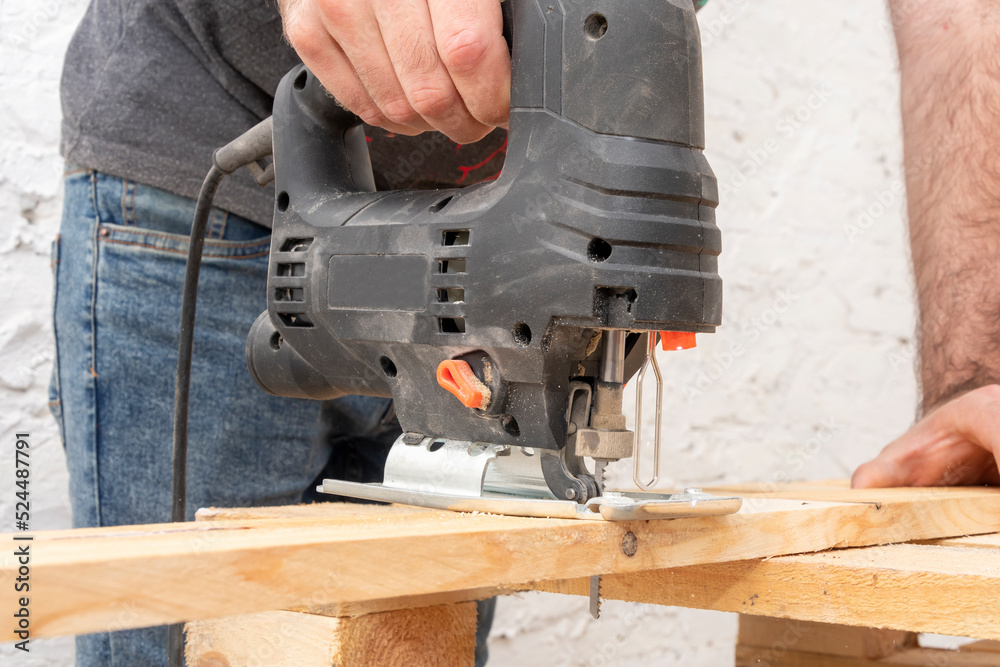 A carpenter cuts a wooden board with an electric jigsaw. Carpentry close-up.