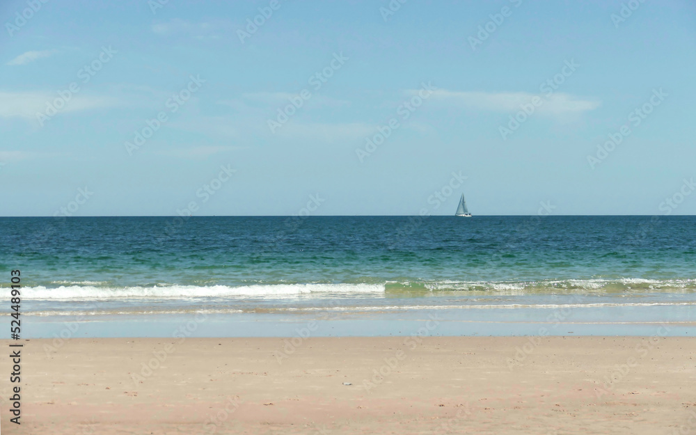 Breezy ocean view with clean sandy coastline and a boat on the horizon 