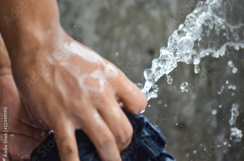 a pair of hands of asian workers rinsing cloth with heavy splashing water in a washing place. hands of the person