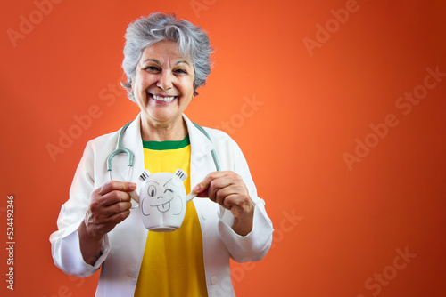 Pediatrician s Day - Mature female doctor with gray hair and child toys isolated on orange background