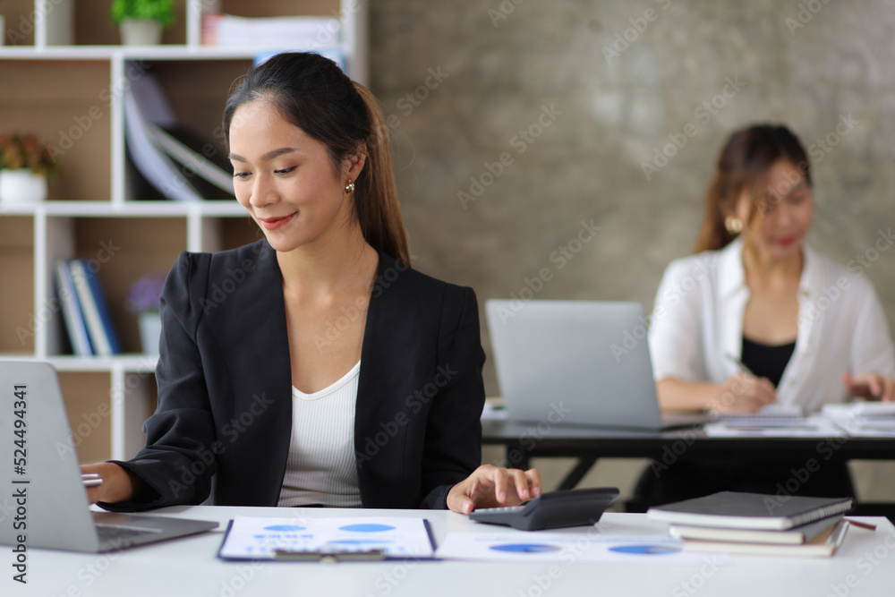 Attractive young beautiful Asian business woman working on laptop and calculating budget by calculator on desk in office. Attractive young beautiful Asian business woman working on laptop and calculating budget by calculator on desk in office.