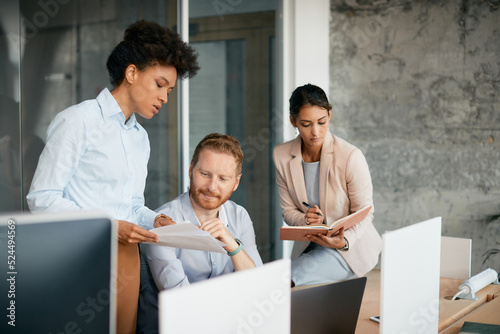 Black businesswoman and her colleagues going through reports on meeting in office. © Drazen