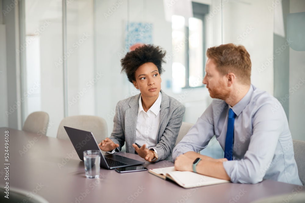 Black female CEO using laptop while talking to colleague in office. Black female CEO using laptop while talking to colleague in office.