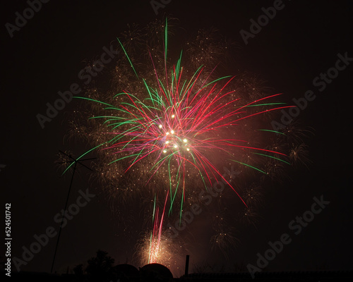 Several bursts of fireworks with rays of red and green light from the center and many sparks on a black background