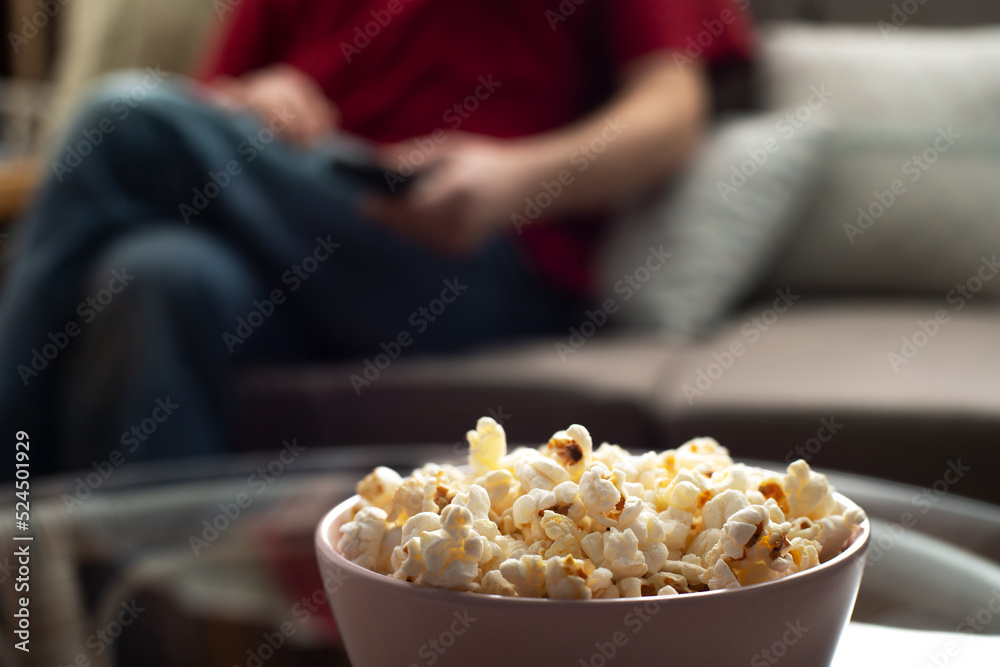 Caucasian man sitting on sofa with popcorn and tv remote Caucasian man sitting on sofa with popcorn and tv remote
