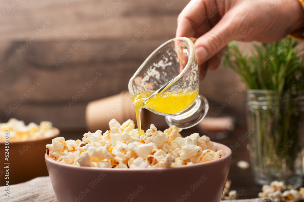 Melted butter being poured on popcorn in clay bowl on kitchen table