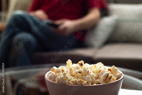 Caucasian man sitting on sofa with popcorn and tv remote