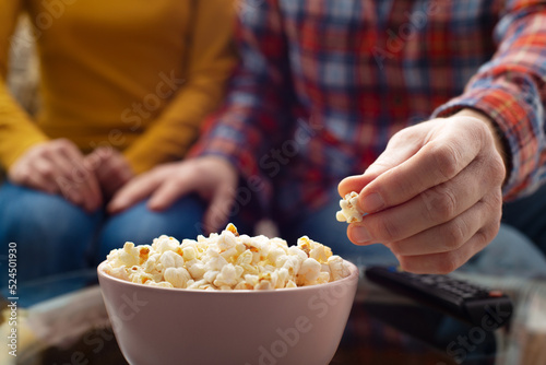 Obraz na płótnie Caucasian couple sitting on sofa with popcorn and tv remote w salonie