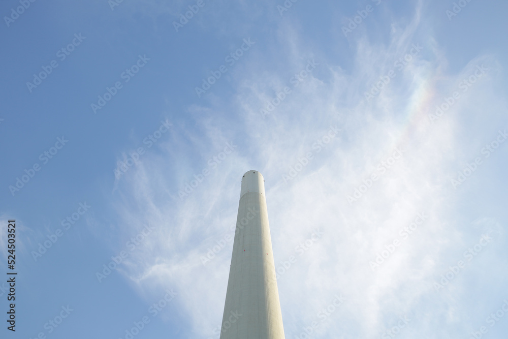A white stone coal power plant chimney with a blue sky and clouds A white stone coal power plant chimney with a blue sky and clouds