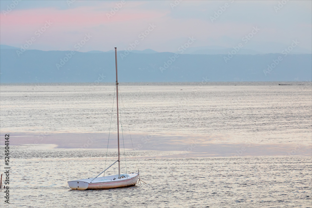 Barca a vela ormeggiata nella laguna del mare adriatico, isola della città di Grado. Paesaggio marino all'alba con visibili le montagne alle prime luci del sole. Barca a vela ormeggiata nella laguna del mare adriatico, isola della città di Grado. Paesaggio marino all'alba con visibili le montagne alle prime luci del sole.