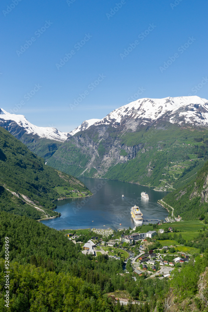 Landscape of the fjord and Geiranger village with high snow-capped mountains and waterfalls, Norway.